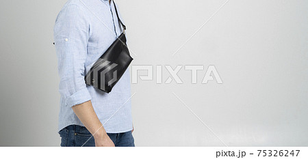 Man in a blue shirt with a leather black handmade bag over his shoulder. Dark designer banana bag. Man in a studio. Comfortable small bag for walking. 75326247