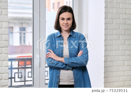 Portrait of young beautiful confident smiling woman in denim shirt with folded arms crossed 75329531