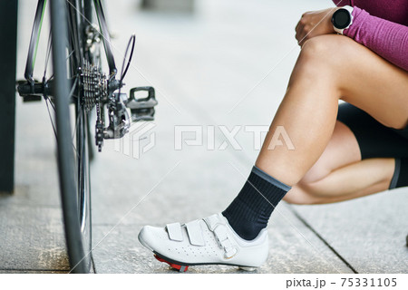 Cropped shot of young sportive woman in cycling shoes checking her bicycle, kneeling outdoors on a daytime 75331105