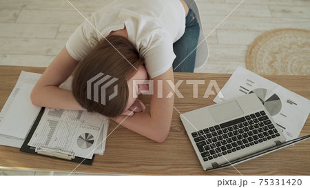 Young tired woman sleeping at her office desk near the laptop 75331420