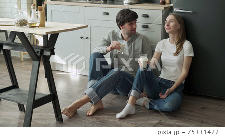 Young couple sits on the floor of their kitchen and drinks delicious milk Young couple sits on the floor of their kitchen and drinks delicious milk 75331422