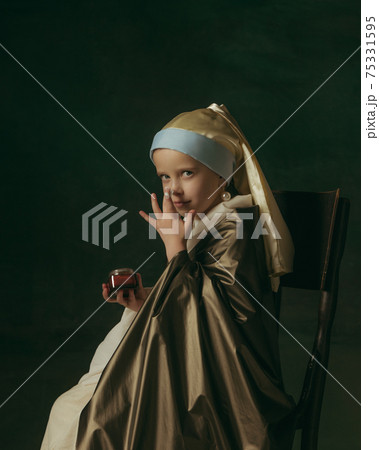 Medieval little girl as a lady with a pearl earring on dark studio background. Concept of comparison of eras, childhood. Stylish creative design, art vision, new look of artwork. 75331595