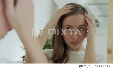 Sad upset woman standing by mirror looking at matted fragile strand in her hand thinking about natural medicinal shampoo restoring hair structure 75331745