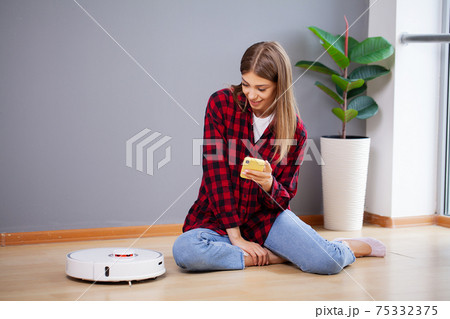Young woman using automatic vacuum cleaner to clean the floor Young woman using automatic vacuum cleaner to clean the floor 75332375