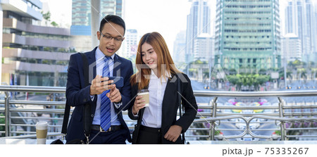 Banner Businessman Businesswoman drinking coffee in town using smartphone outside office city. Panorama Hands holding take away coffee cup, smart phone talking together Business partner copyspace 75335267