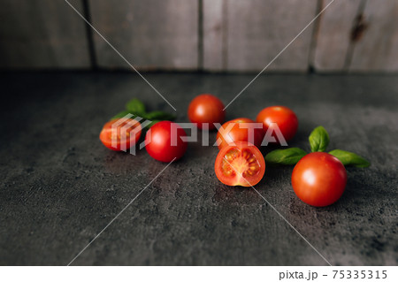 Red cherry tomatoes with green basil on a gray background 75335315
