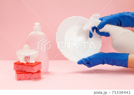 Women's hands in rubber gloves with a bottle of dishwashing liquid and a plate on the pink background. 75336441
