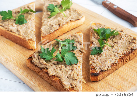 Sandwiches crispy toast and chicken liver pate with parsley leaves on a wooden cutting board. 75336854