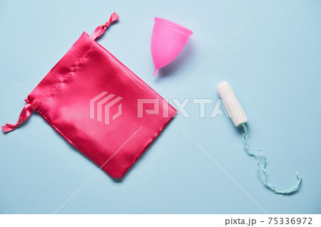 Pink menstrual cup and variuos of tampons on blue background 75336972