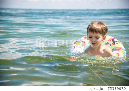Happy little boy playing with colorful inflatable ring in outdoor swimming sear river lake or pool on hot summer day. Kids learn to swim and having fun 75339070
