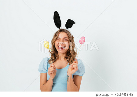 Cheerful young blonde woman wears Easter bunny ears holding decorative colored eggs Cheerful young blonde woman wears Easter bunny ears holding decorative colored eggs 75340348