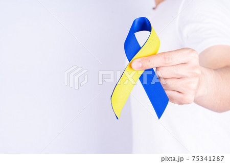 Down syndrome day, hands holding blue yellow ribbon awareness on chest support patient with illness disability 75341287