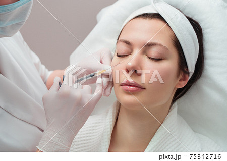 The doctor cosmetologist makes the rejuvenating facial injections procedure for tightening and smoothing wrinkles on the face skin of a beautiful, young woman in a beauty salon. Cosmetology, skincare The doctor cosmetologist makes the rejuvenating facial injections procedure for tightening and smoothing wrinkles on the face skin of a beautiful, young woman in a beauty salon. Cosmetology, skincare 75342716
