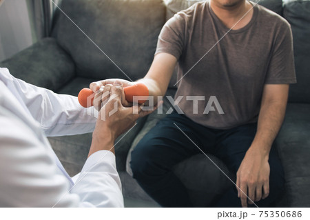 Asian young male physiotherapist helping patient with lifting dumbbells exercises in office. 75350686