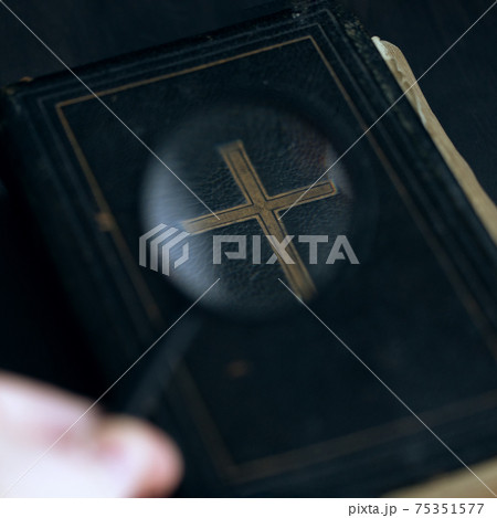 Vintage antique bible book on table and magnifying glass in human hand. 75351577