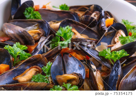 Boiled mussels in cooking dish with parsley on a wooden background Boiled mussels in cooking dish with parsley on a wooden background 75354175