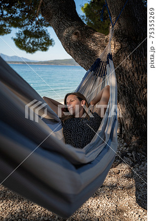 Woman lying in a hammock under a pine tree by the sea Woman lying in a hammock under a pine tree by the sea 75355269
