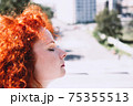 Face of young beautiful woman close-up on the street. Female with curly, red hair, eyes closed 75355513