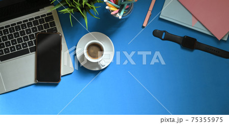 Top view image of computer laptop putting on colorful working desk with coffee cup, potted plant, pencils in glass vase, smartphone, note, smartwatch and notebook. Orderly workspace concept. Top view image of computer laptop putting on colorful working desk with coffee cup, potted plant, pencils in glass vase, smartphone, note, smartwatch and notebook. Orderly workspace concept. 75355975