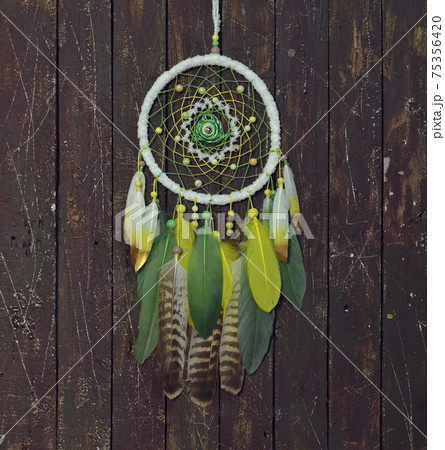 Beautiful handmade boho dreamcatcher with green, yellow and white feathers and medalion. Mystic background with dream catcher against wooden planks, esoteric, ethnic and spiritual concept Beautiful handmade boho dreamcatcher with green, yellow and white feathers and medalion. Mystic background with dream catcher against wooden planks, esoteric, ethnic and spiritual concept 75356420
