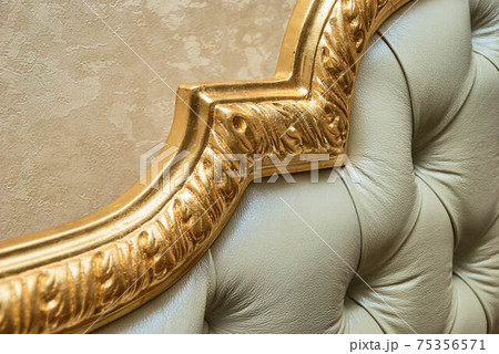 Headboard of beige leather and carved golden molding closeup Headboard of beige leather and carved golden molding closeup 75356571