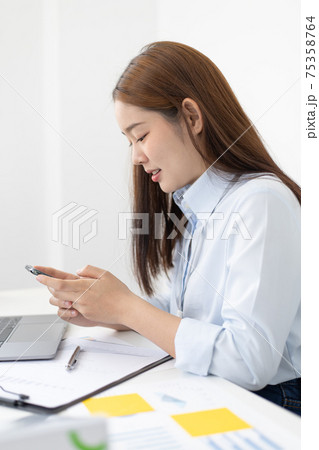 Asian female employees are analyzing market data via smartphones and have laptops to calculate the company's finances In a private office at home, Working at home and new normal concept. 75358764