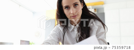 Serious woman is sitting in office at table and holding documents. Serious woman is sitting in office at table and holding documents. 75359718