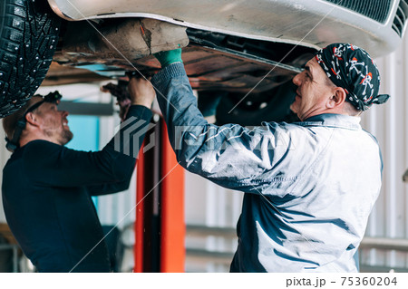 Auto mechanics remove the underbody protection of an internal combustion engine on a car. Scheduled maintenance and oil change of the machine 75360204