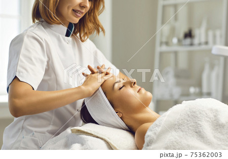 Cosmetologist or dermatologist making facial beauty massage treatment for young woman in beauty spa salon with fingers 75362003