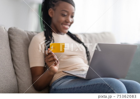 Closeup of positive black woman holding credit card, using laptop 75362083