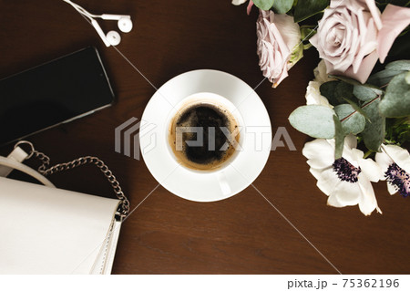 Cup of coffee, bouquet of anemone, purple roses, woman handbag, phone on table Cup of coffee, bouquet of anemone, purple roses, woman handbag, phone on table 75362196