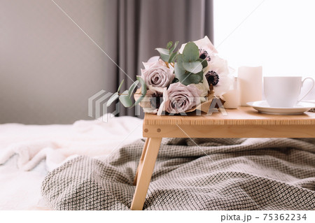 Coffee table on bed. Flowers, coffee cup and candles. Interior gray tones, plaid 75362234