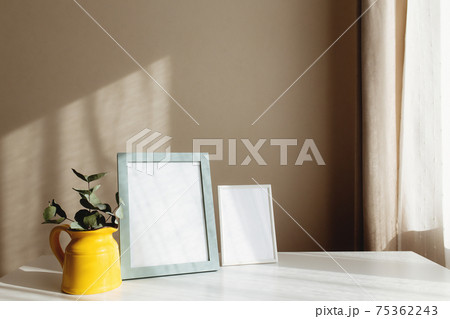 Yellow ceramic jug or vase with eucalyptus branches, empty white photo frames 75362243