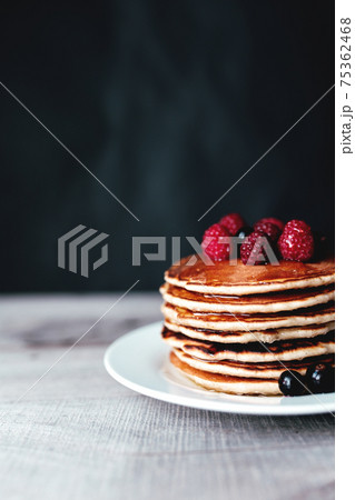 Juicy pancakes with berries and honey on a white plate, spoon, wooden table Juicy pancakes with berries and honey on a white plate, spoon, wooden table 75362468