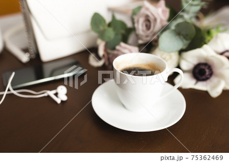Cup of coffee, bouquet of anemone, purple roses, woman handbag, phone on table 75362469