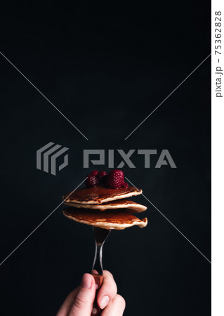 Hand holds a fork with juicy pancakes with berries and honey Hand holds a fork with juicy pancakes with berries and honey 75362828