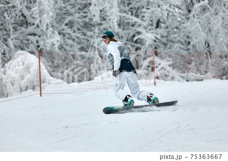 cheerful woman riding on snowboard in the mountains in winter. woman in white ski suit cheerful woman riding on snowboard in the mountains in winter. woman in white ski suit 75363667