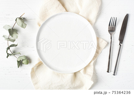 An empty plate and cutlery on a white table. 75364236