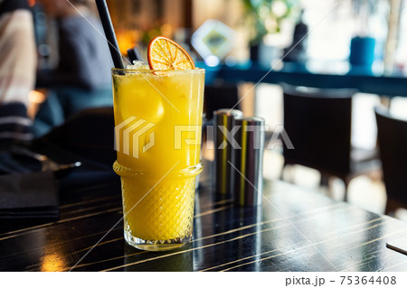 Glass with tasty juicy bright yellow citrus orange lemonade cocktail on dark wooden table at cafe or restaurant on brigh sunny morning day. Nonalcoholic party drink. Hipster lifestyle background 75364408
