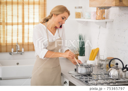 Blonde woman stirring something in a saucepan and talking on the phone 75365797