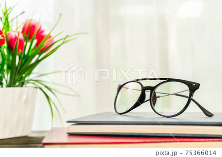 Reading glasses put on hardcover book beside the window Reading glasses put on hardcover book beside the window 75366014