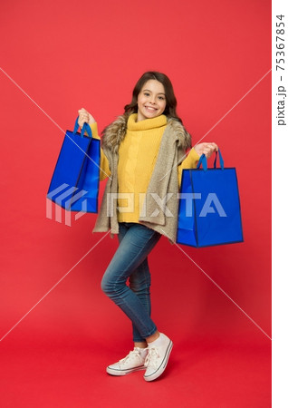 Happy little girl with fashion look carry shopping bags red background, sale 75367854
