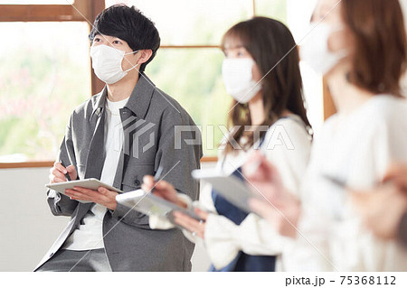 タブレットでメモをとるマスク装着の若い男性 75368112