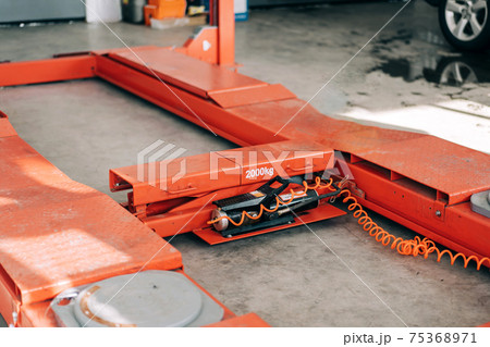 Orange car lift in a calm state for indoor use. Equipment at the service station for lifting machines Orange car lift in a calm state for indoor use. Equipment at the service station for lifting machines 75368971