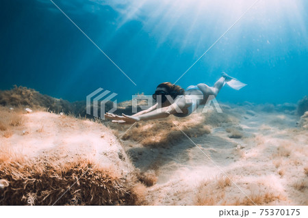 Freediver woman with fins glides at deep sea. Freediving underwater in sea Freediver woman with fins glides at deep sea. Freediving underwater in sea 75370175