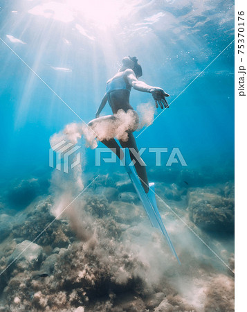Freediver woman glides with sand in hand. Free diver with fins posing underwater Freediver woman glides with sand in hand. Free diver with fins posing underwater 75370176