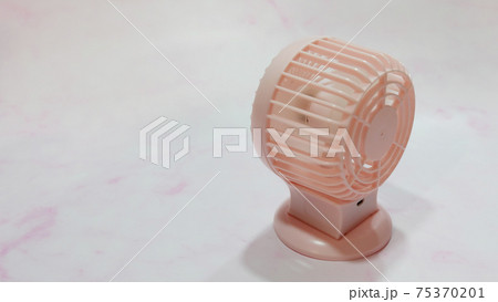 A small pink portable fan, on a pink marble-like surface. 75370201