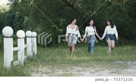 Three pretty brunette girlfriends going on the grass holding hands 75371216