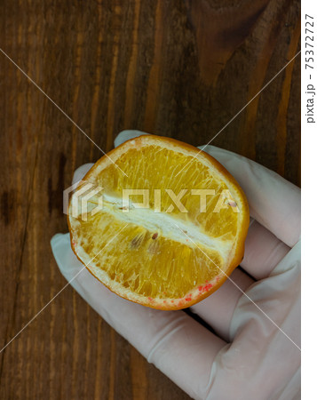 Ugly food trend. Spoiled yellow lemon half with red mold on wooden background. Moldy citrus penicillin inedible fruit 75372727