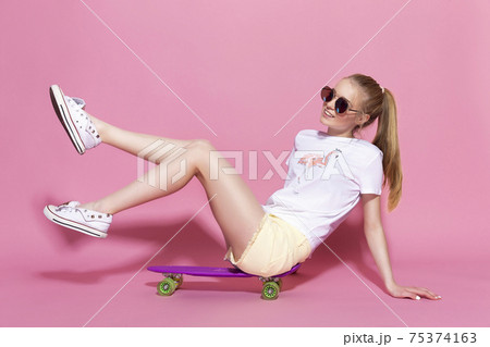 Cheerful young girl with a skateboard on the pink background Cheerful young girl with a skateboard on the pink background 75374163